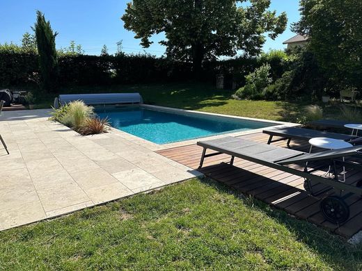 Piscine à l'eau bleue, entourée de pelouse et chaises longues, dans un cadre extérieur ensoleillé.