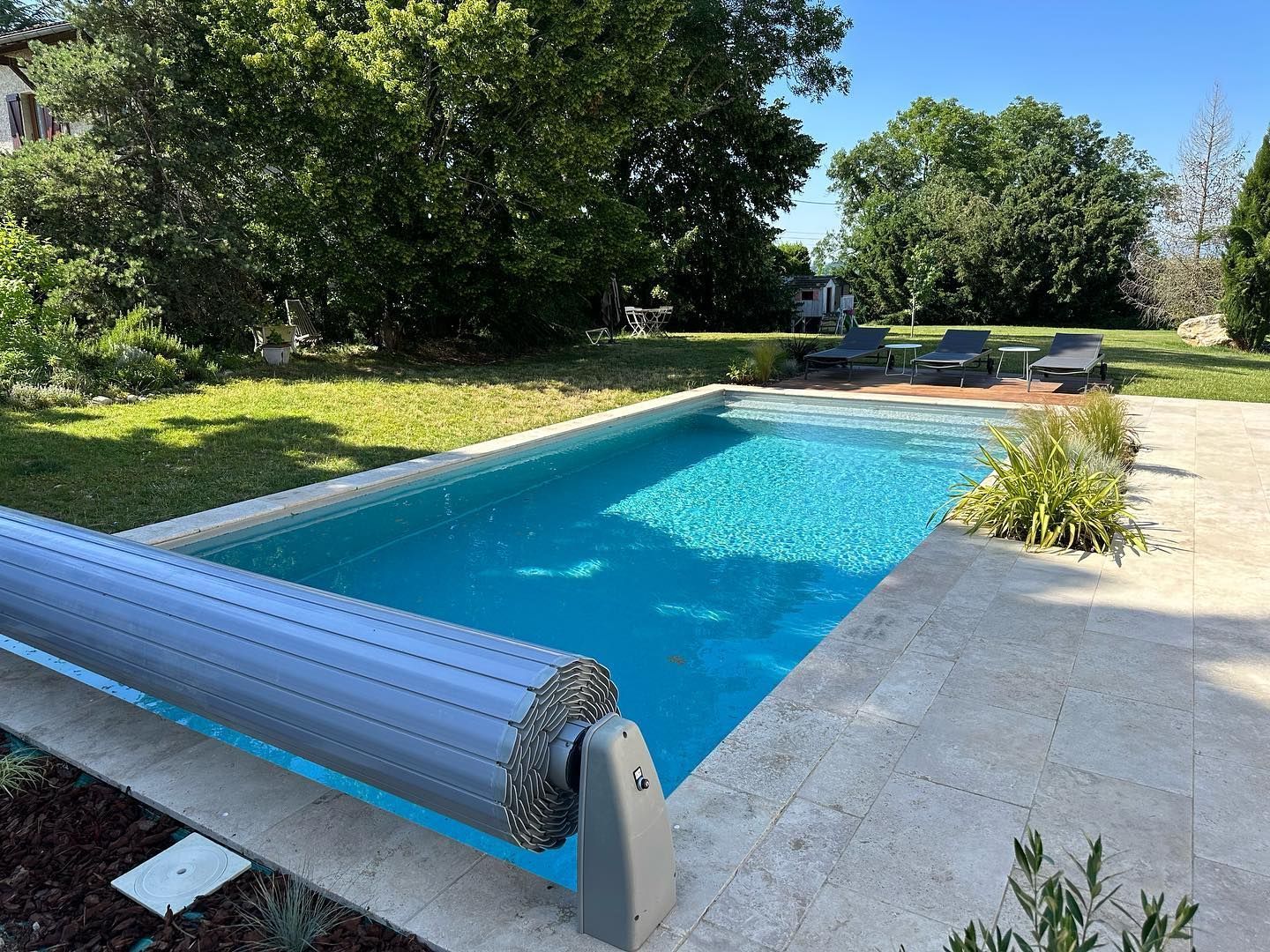 Une piscine rectangulaire à l'eau bleu claire, entourée d'une terrasse et d'une pelouse verte.