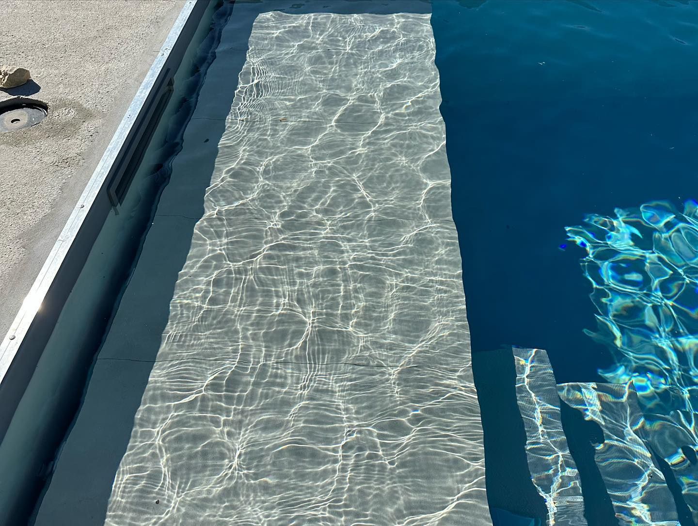 Marches de piscine descendant dans l'eau bleue, reflets chatoyants.