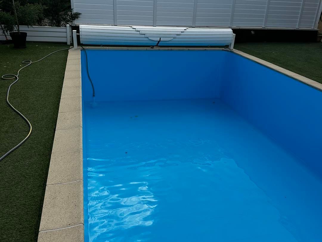 Piscine rectangulaire bleue avec couverture partiellement ouverte, entourée de gazon artificiel.