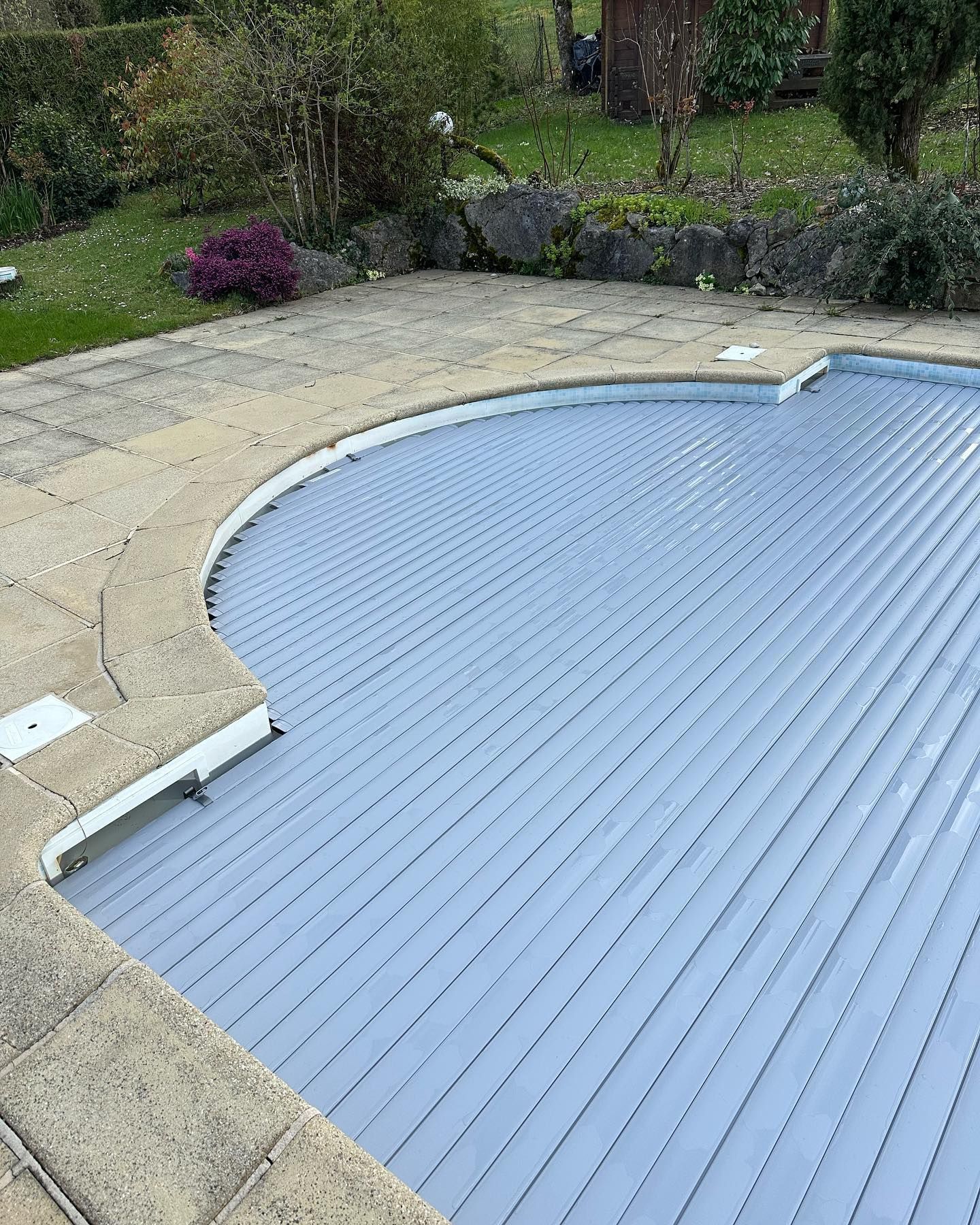 Piscine recouverte d'une protection grise à motifs linéaires.