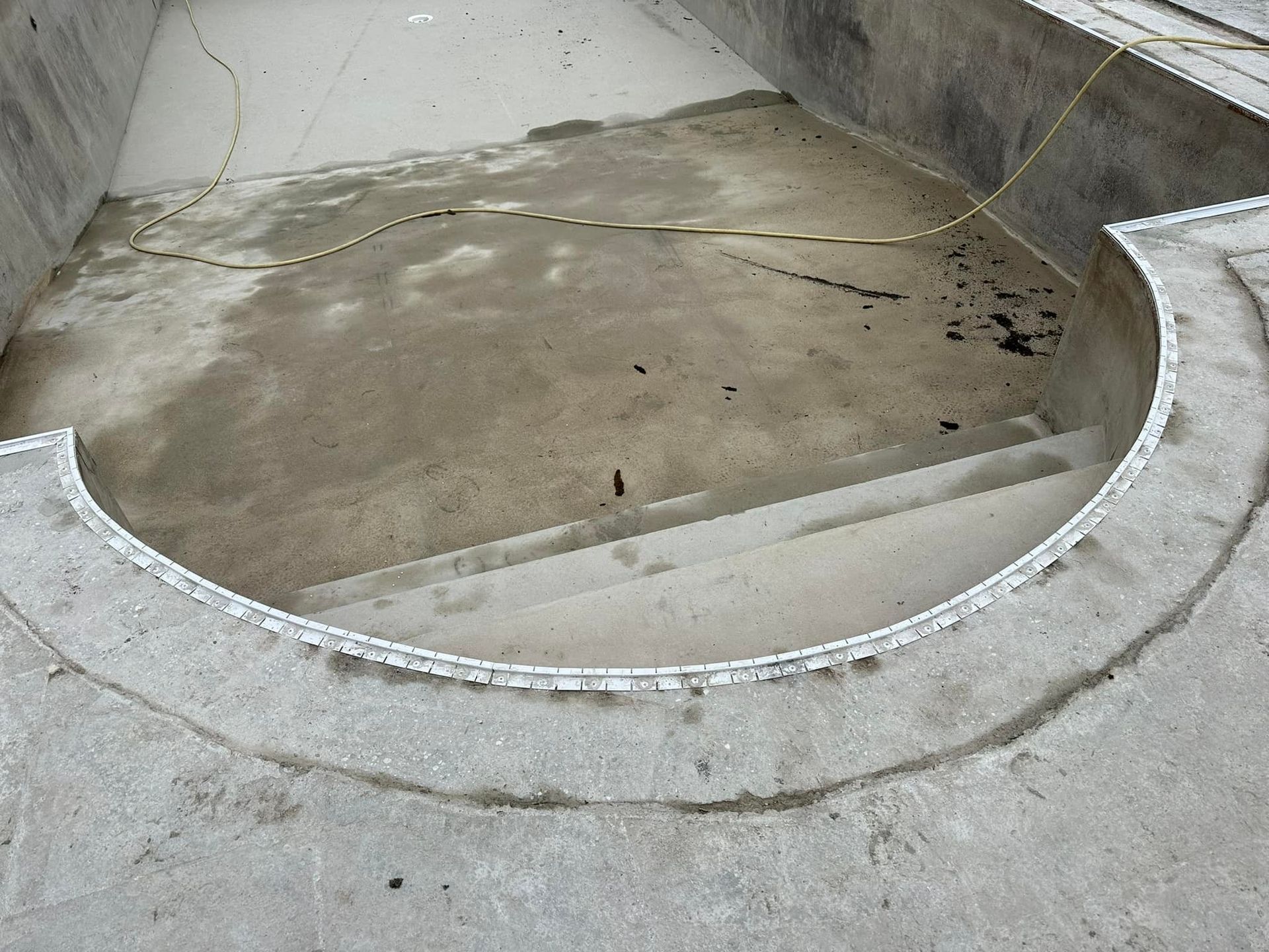 Piscine en béton vide avec marches courbes, nécessitant une rénovation.