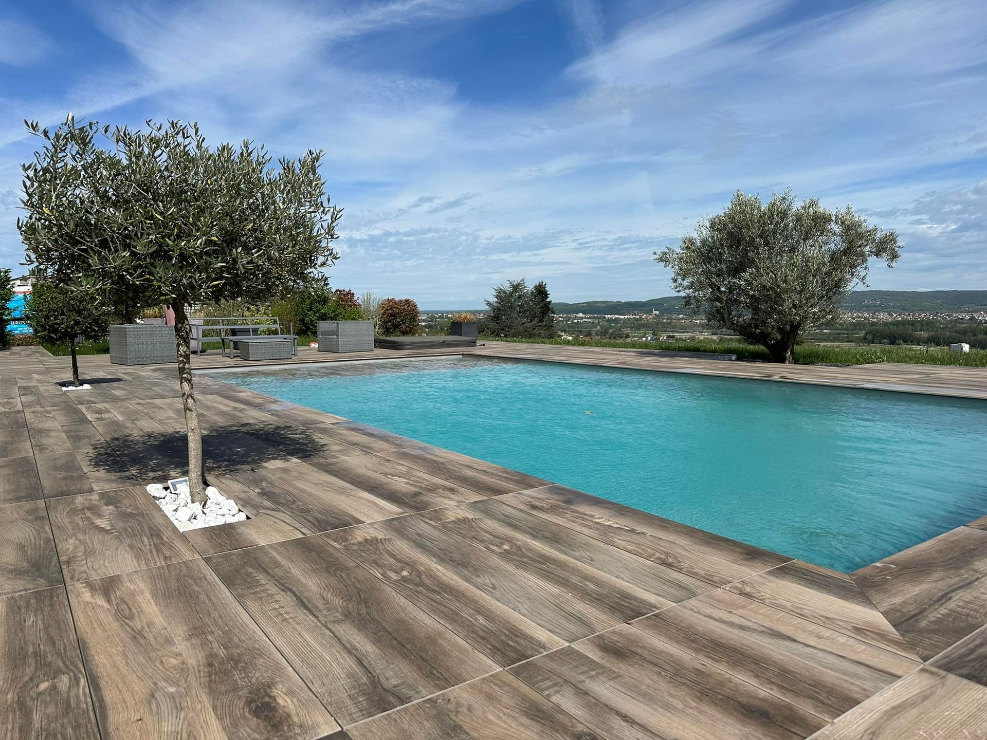 Piscine donnant sur une vue panoramique avec des arbres, un ciel clair et une terrasse en bois.