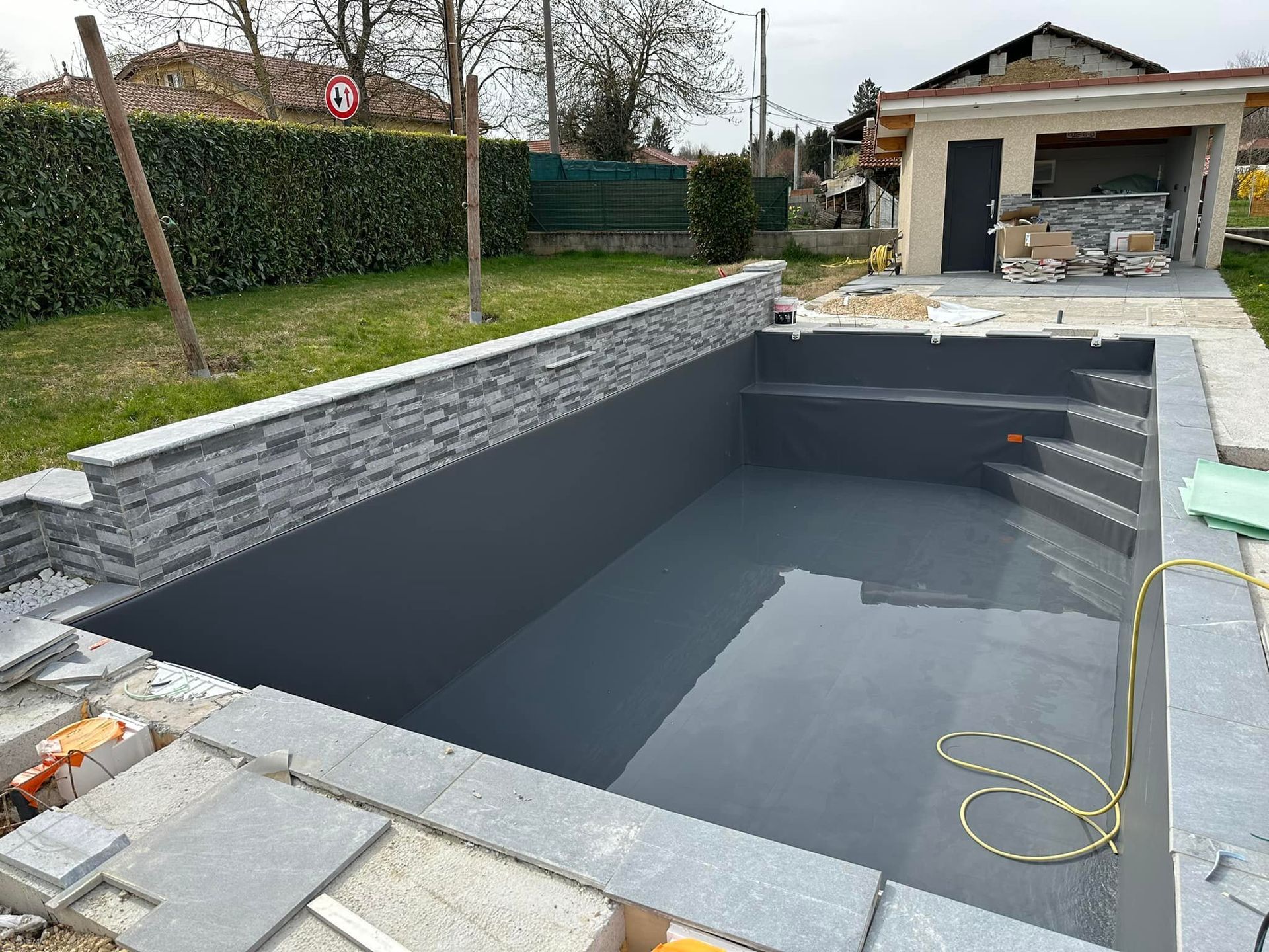 Piscine rectangulaire nouvellement construite avec intérieur gris et bordure en pierre.