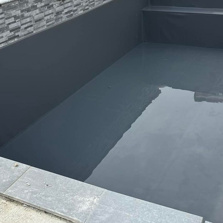 Piscine grise vide avec marches et bordure en pierre.