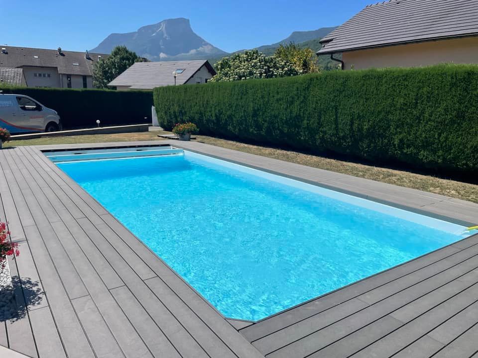 Piscine extérieure rectangulaire avec eau bleue et terrasse grise, adossée à des haies vertes et une vue sur la montagne.