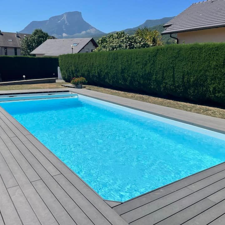 Une piscine rectangulaire avec de l'eau bleue et une terrasse grise, dans une cour arrière avec vue sur la montagne.