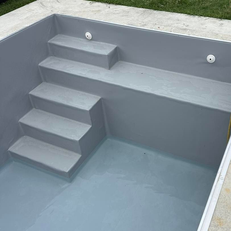 Piscine grise en construction avec marches intégrées, eau au fond, installée en extérieur.