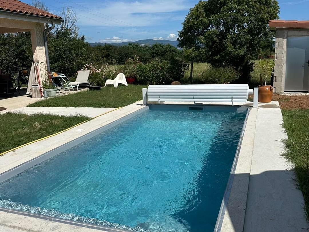 Piscine rectangulaire avec eau bleue et couverture blanche avec une maison en arrière-plan.