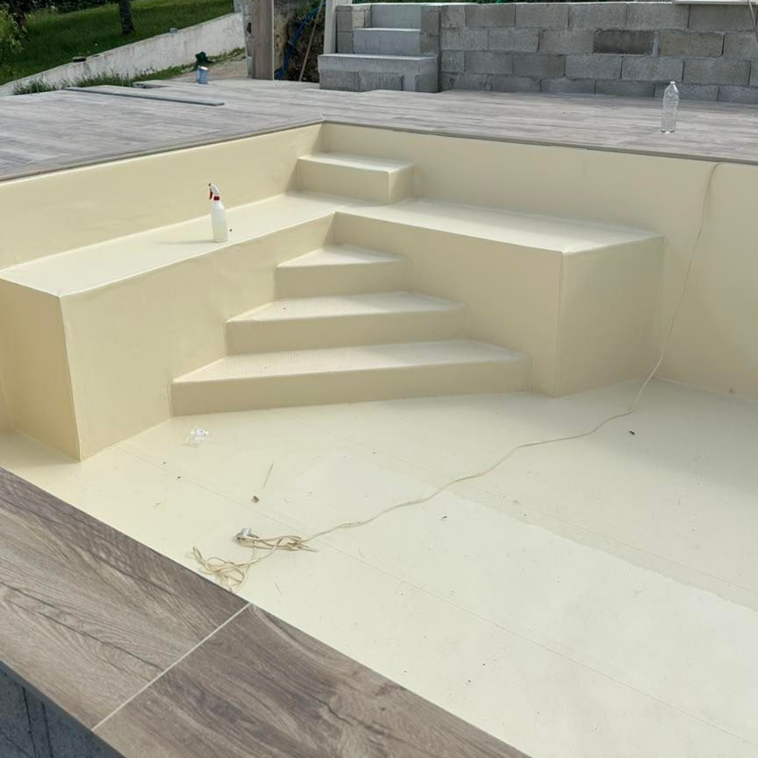 Une piscine vide avec escalier intégré, peinte en beige, sur une terrasse carrelée.