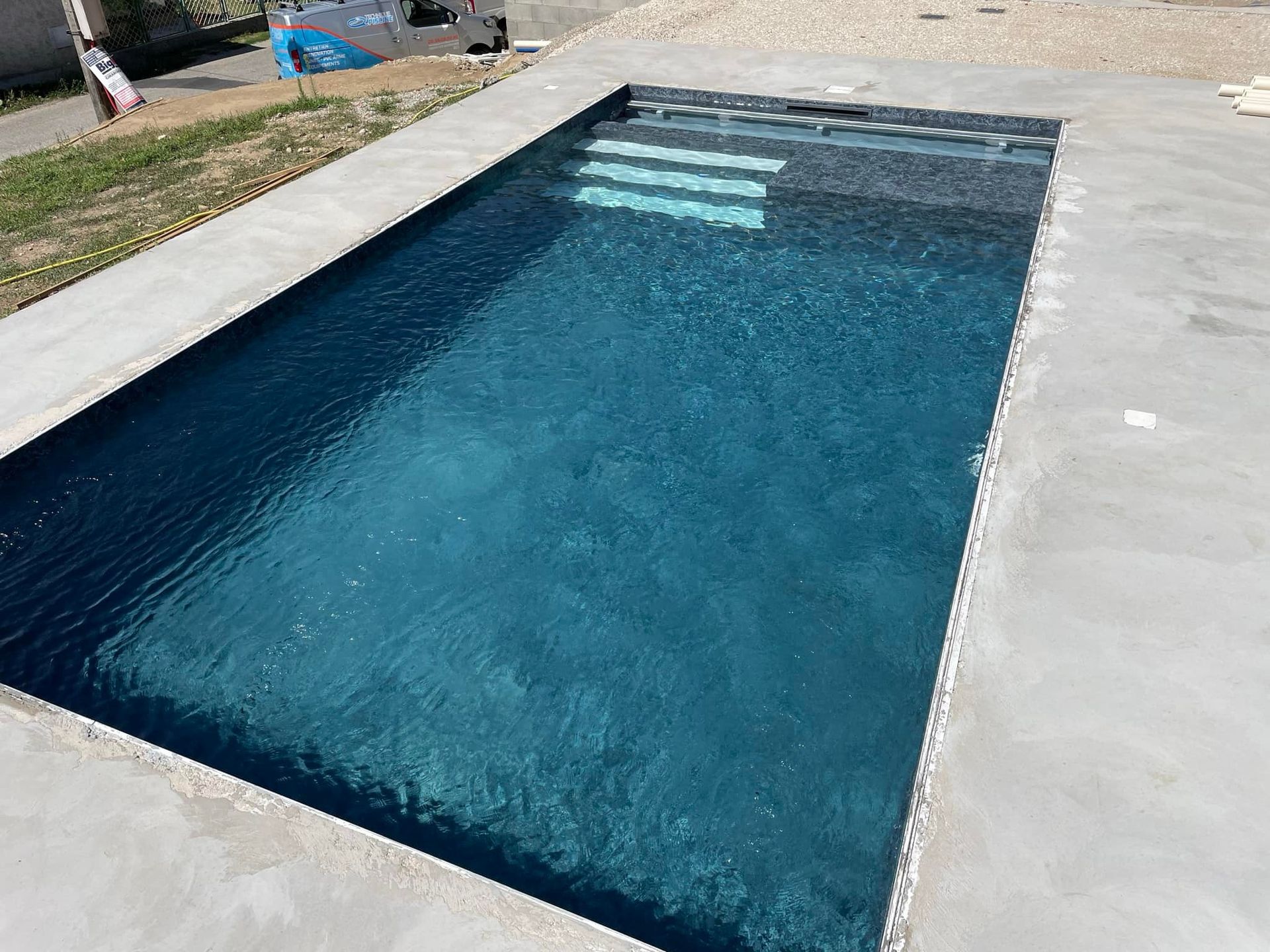 Une piscine rectangulaire avec eau bleue, marches intégrées et margelle en béton.