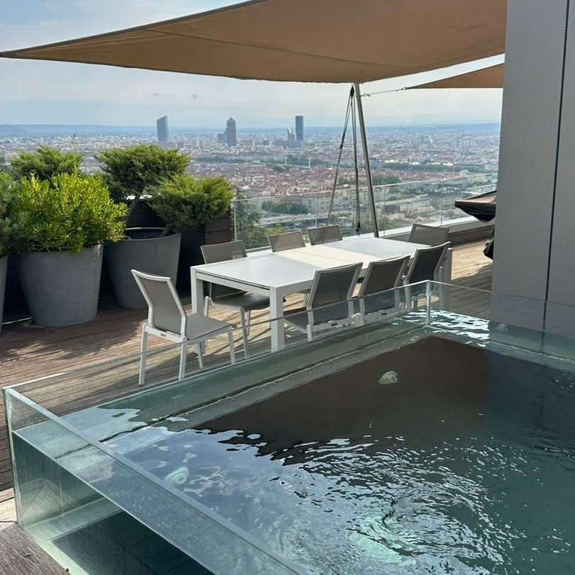 Vue d'une ville avec piscine vitrée sur une terrasse en bois en haut d'un appartement.