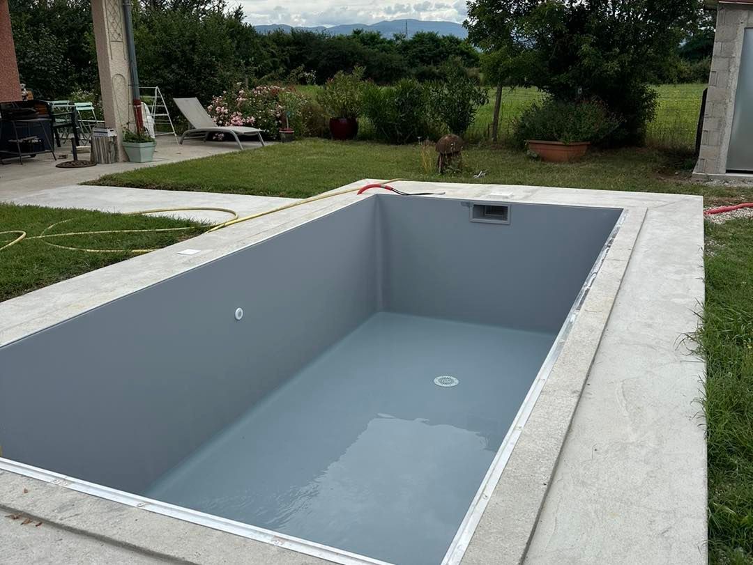 Piscine rectangulaire vide avec intérieur gris, entourée d'une bordure en béton et d'herbe verte.