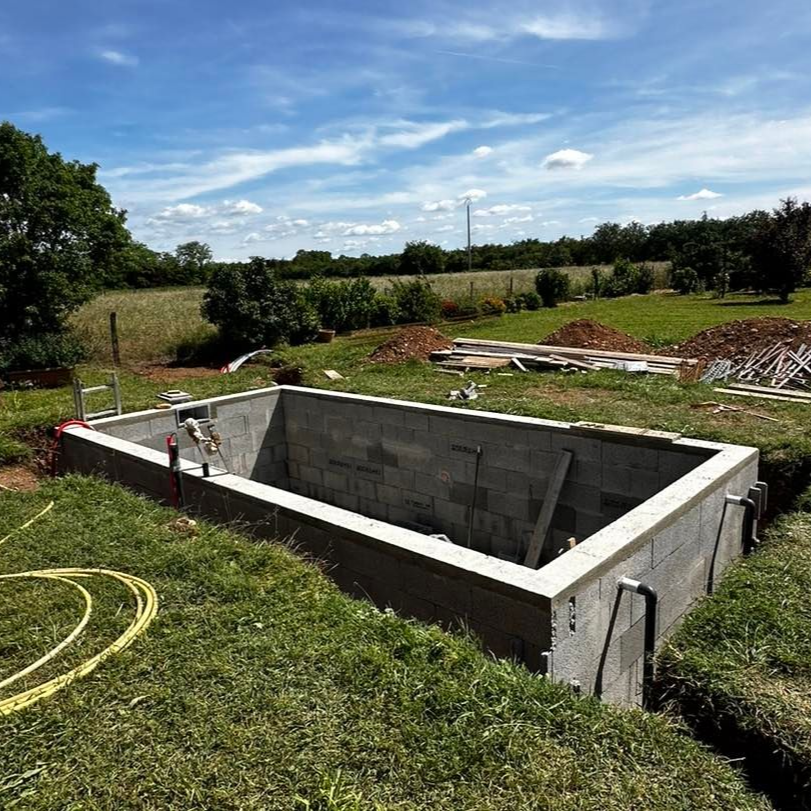 Une piscine en béton en construction dans un champ herbeux par une journée ensoleillée.
