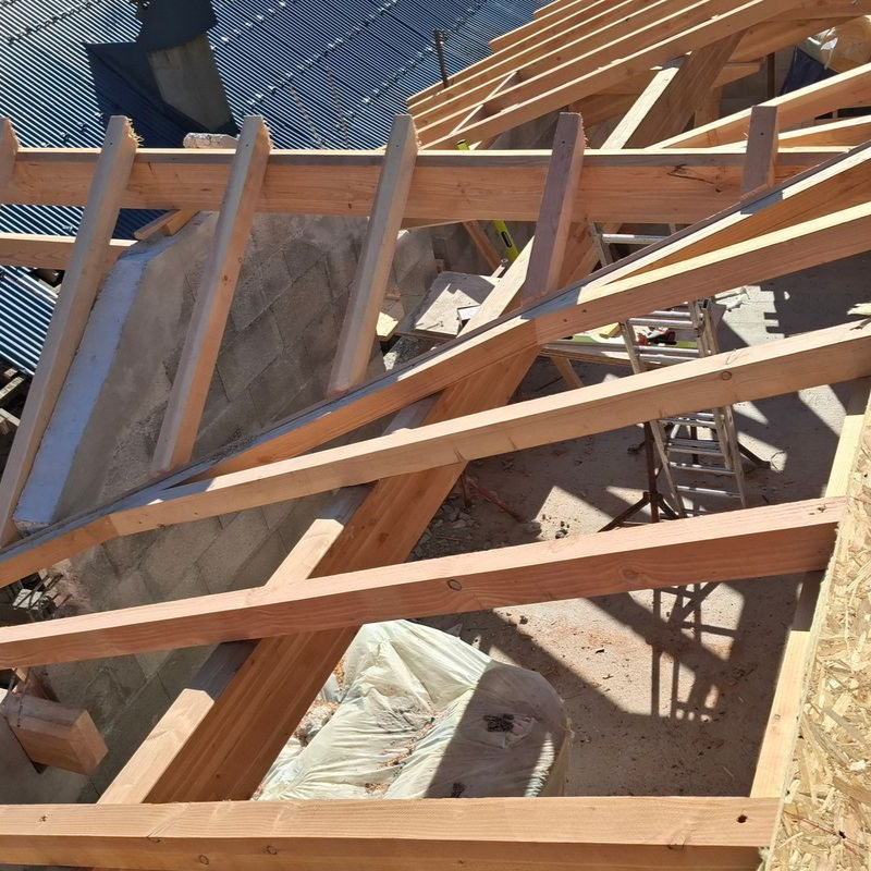 Charpente en bois en construction sur une fondation de maison en béton.