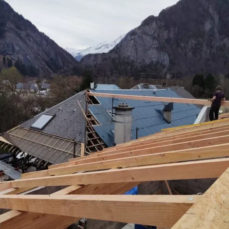 Ouvrier du bâtiment sur un toit avec poutres en bois, arrière-plan de montagne.