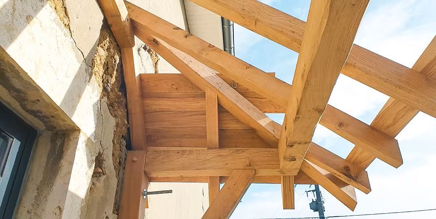 Des poutres en bois forment l'ossature d'un porche, adossée à un mur en stuc patiné par les intempéries.