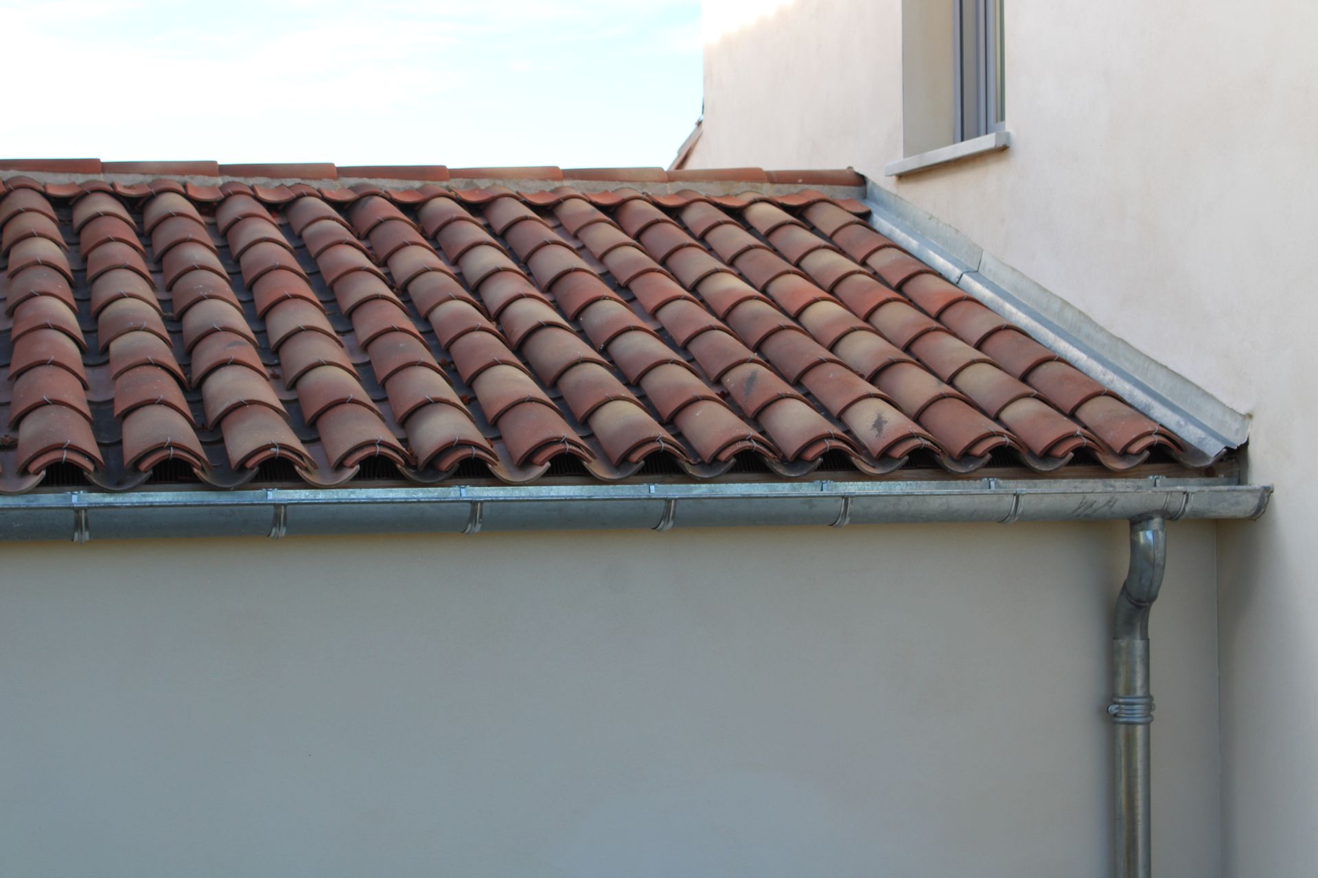 Toit en tuiles rouges avec une gouttière en métal à côté d'un mur blanc.