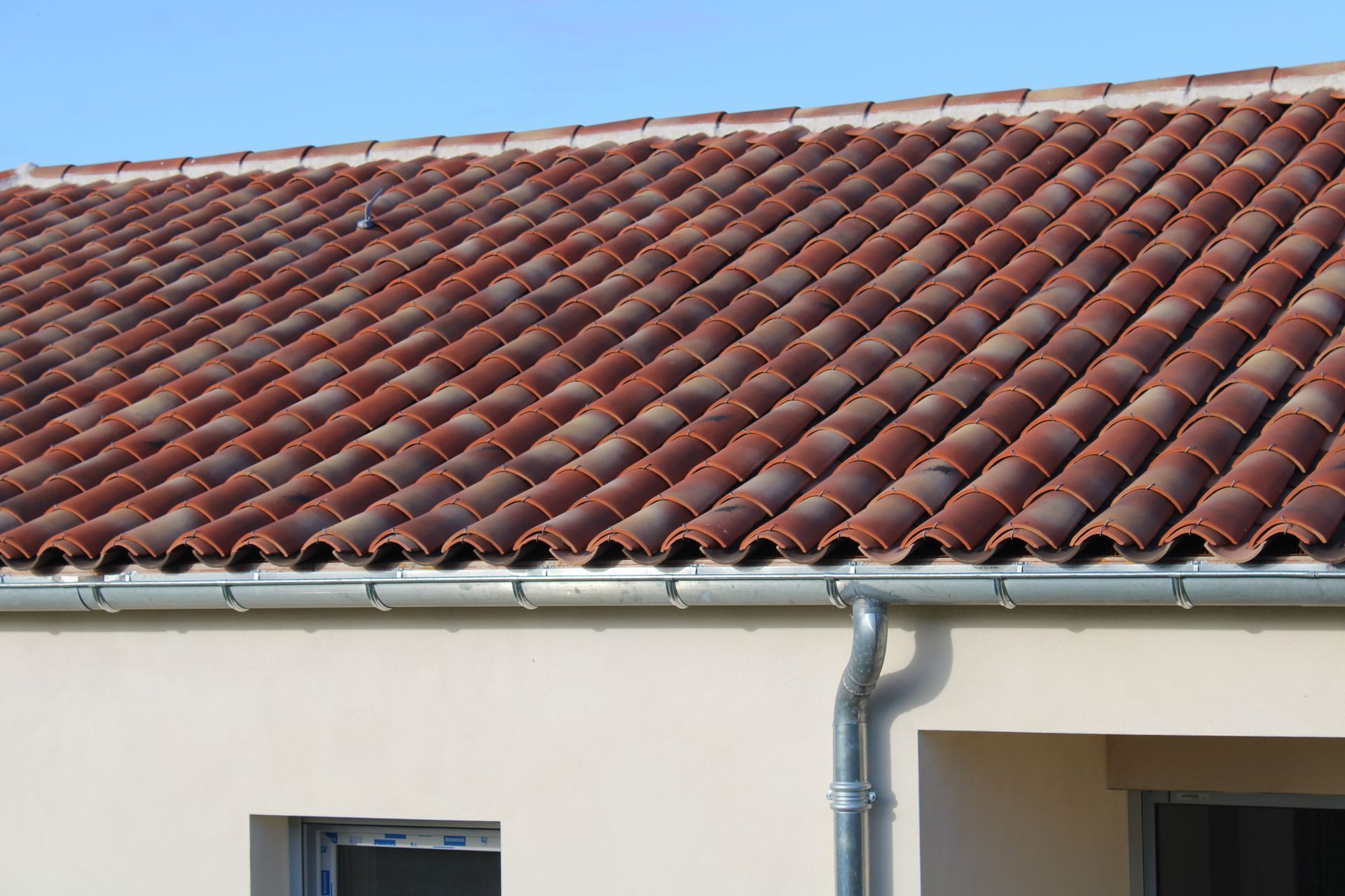 Toit de tuiles rouges avec gouttière sur un bâtiment de couleur claire.