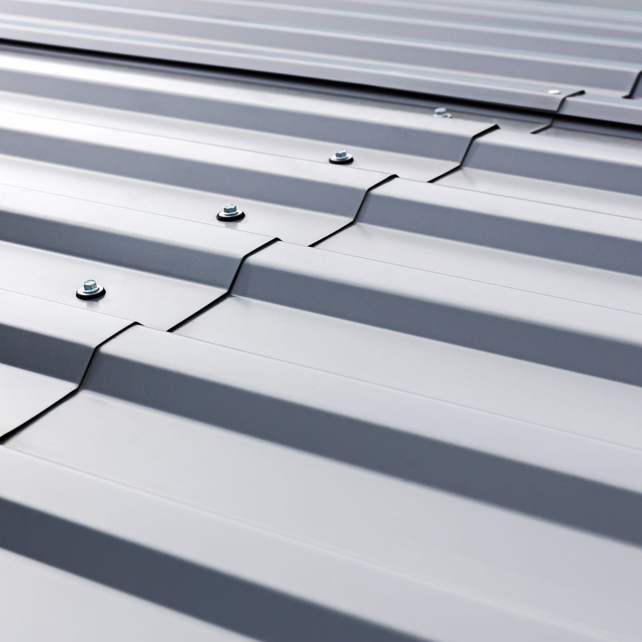 Gros plan d'un toit en métal gris avec des panneaux ondulés, fixés par des boulons.
