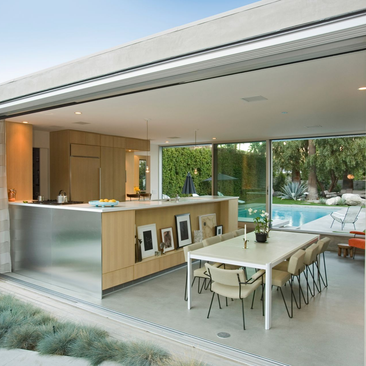 Cuisine ouverte avec îlot en acier inoxydable, table à manger et vue sur la piscine.