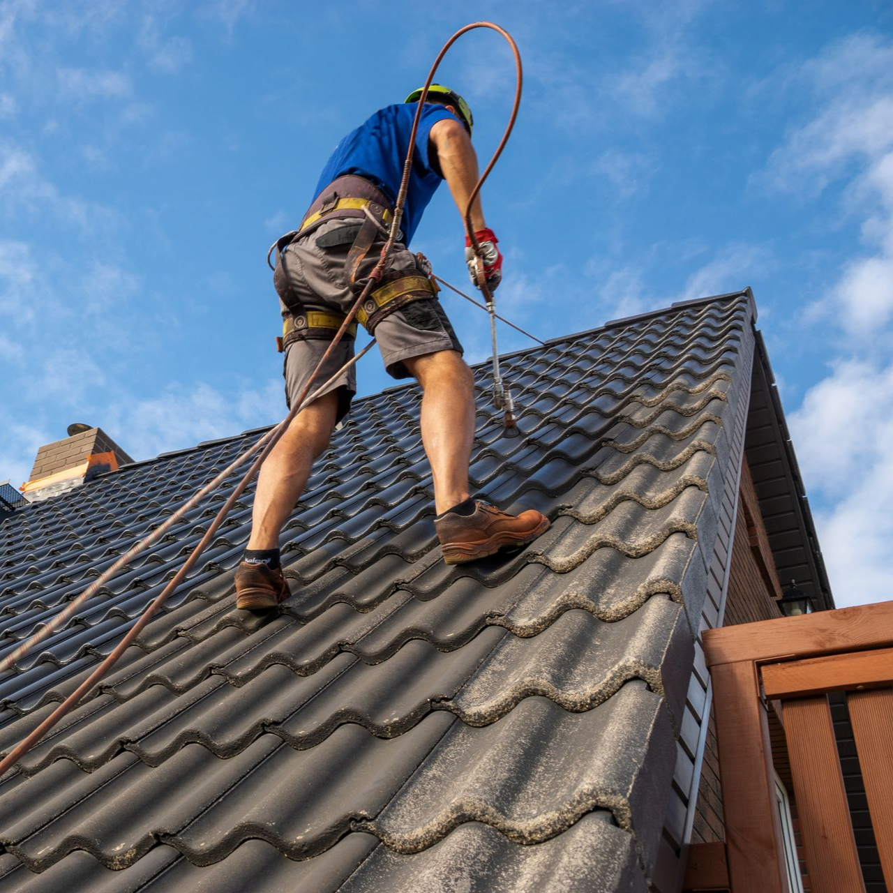 Un couvreur nettoyant des tuiles au jet à haute pression.