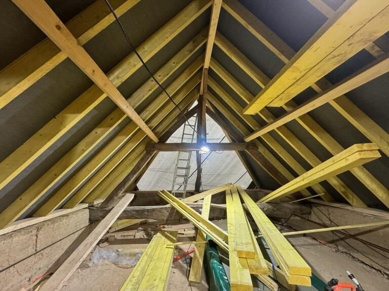 Vue de l'intérieur d'un grenier avec chevrons en bois apparents, isolation et matériaux de construction.