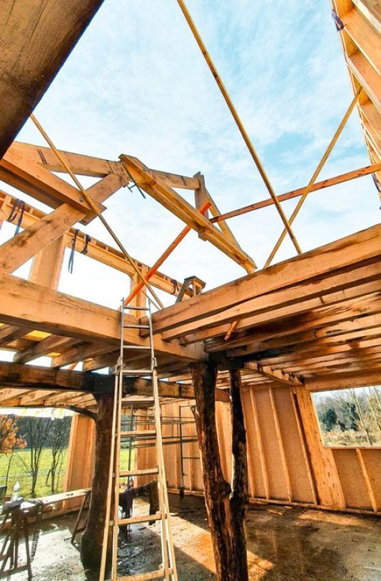 Construction d'une maison à ossature en bois avec échelles et poutres de support contre un ciel bleu.