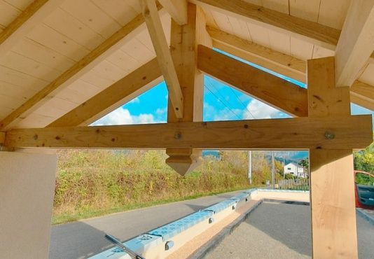 Des poutres en bois soutiennent un toit, encadrant une vue sur une piscine couverte.