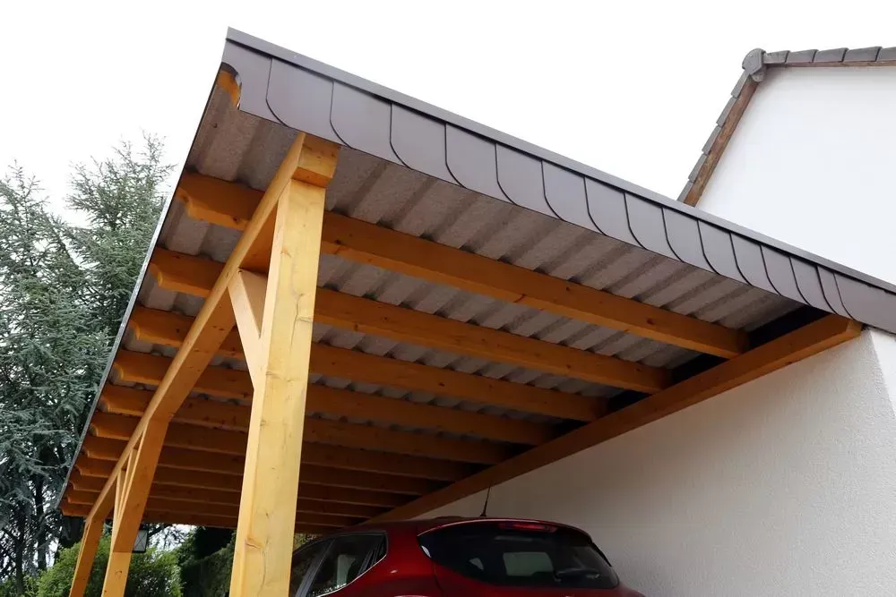 Carport avec ossature en bois et une voiture rouge garée en dessous.