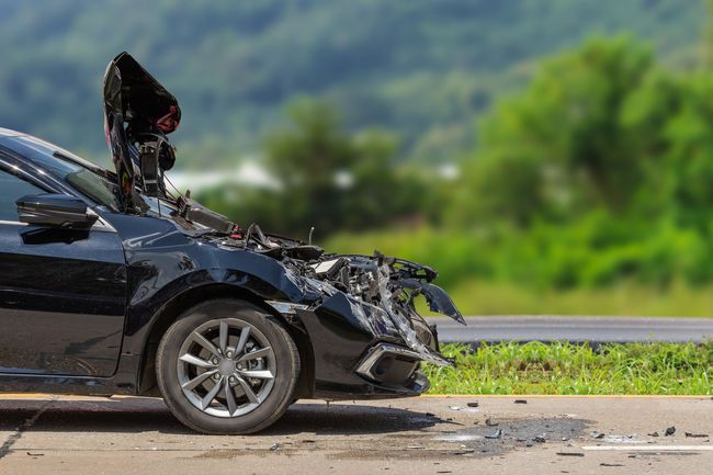 Un coche negro con el parabrisas roto está estacionado al costado de la carretera.