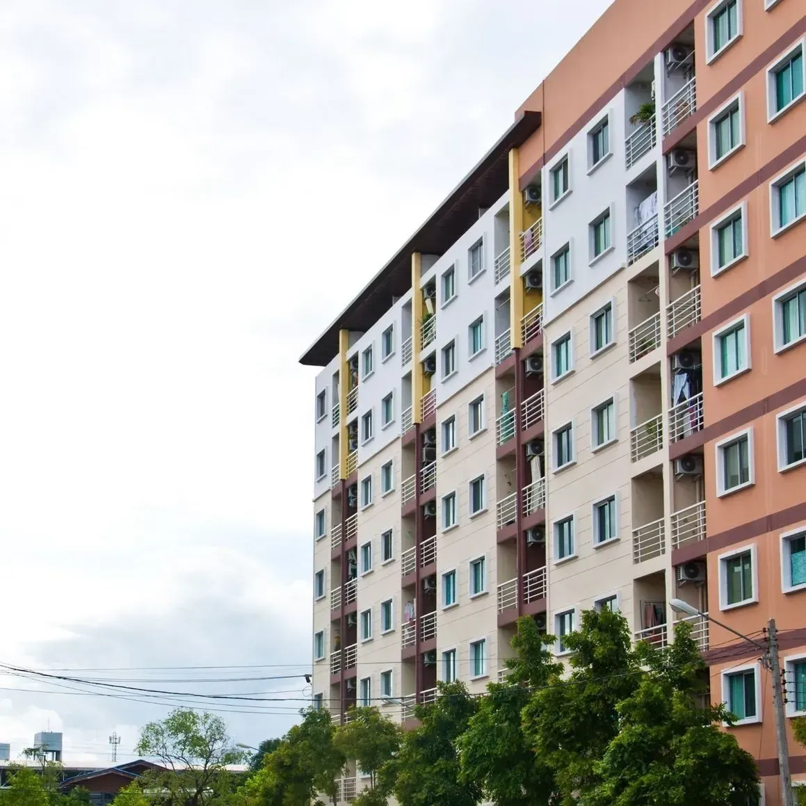Edificio de apartamentos de varias plantas con fachada naranja, blanca y beige. Árboles verdes en primer plano.