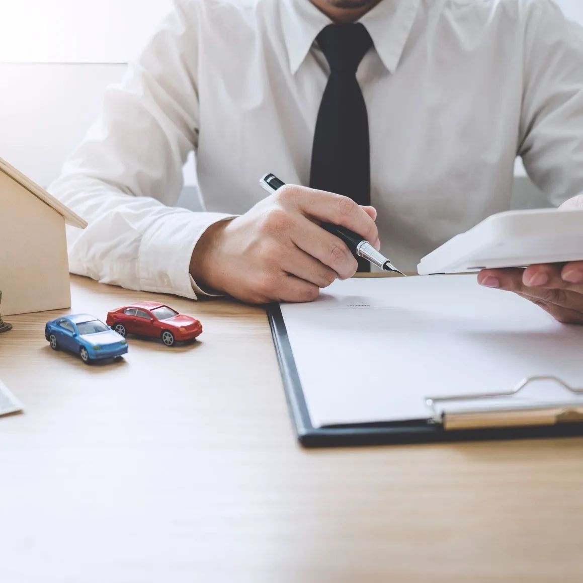 Persona con camisa blanca y corbata negra haciendo cálculos con calculadora, con coches de juguete.