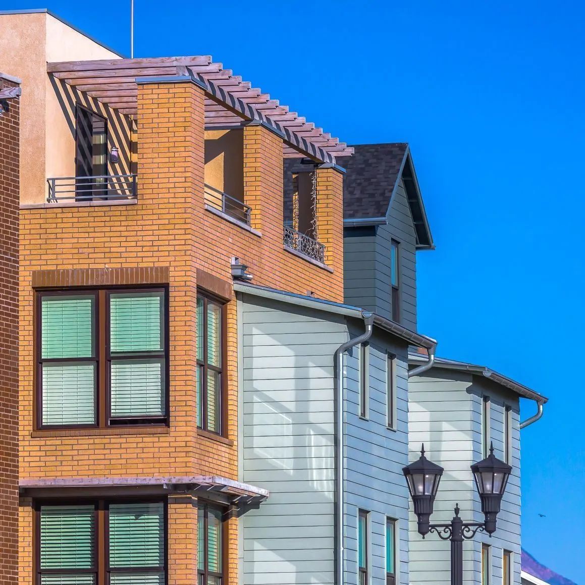 Hilera de casas adosadas con exteriores de ladrillo y revestimiento contra un cielo azul brillante.
