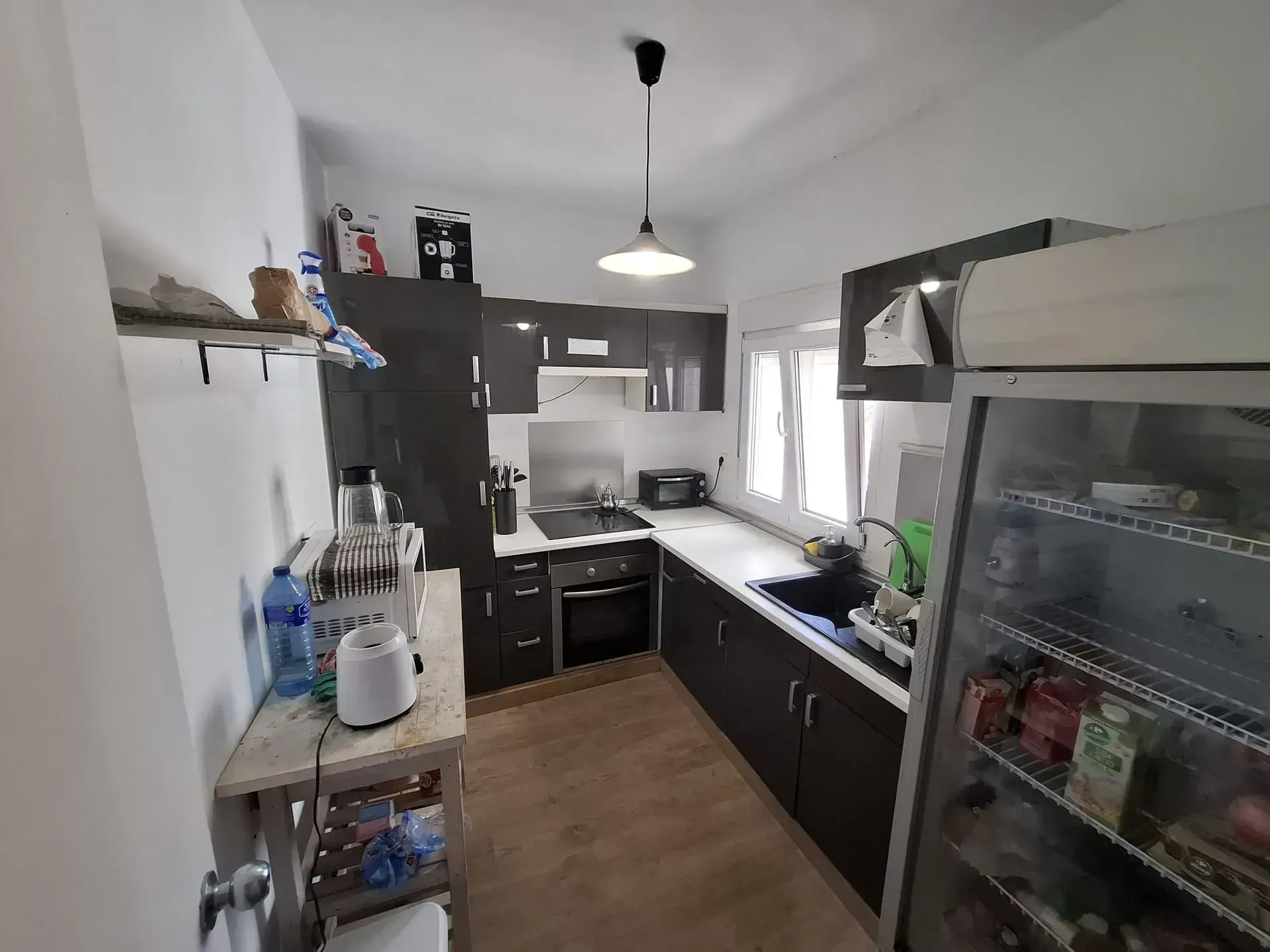 Cocina pequeña con gabinetes oscuros, electrodomésticos de acero inoxidable y una ventana.