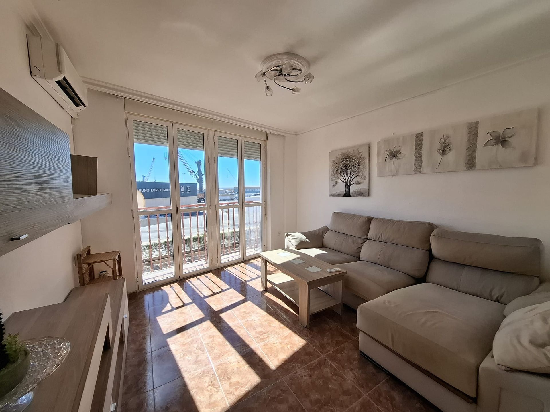 Sala de estar con sofá seccional color bronce, puertas corredizas de vidrio y luz solar.