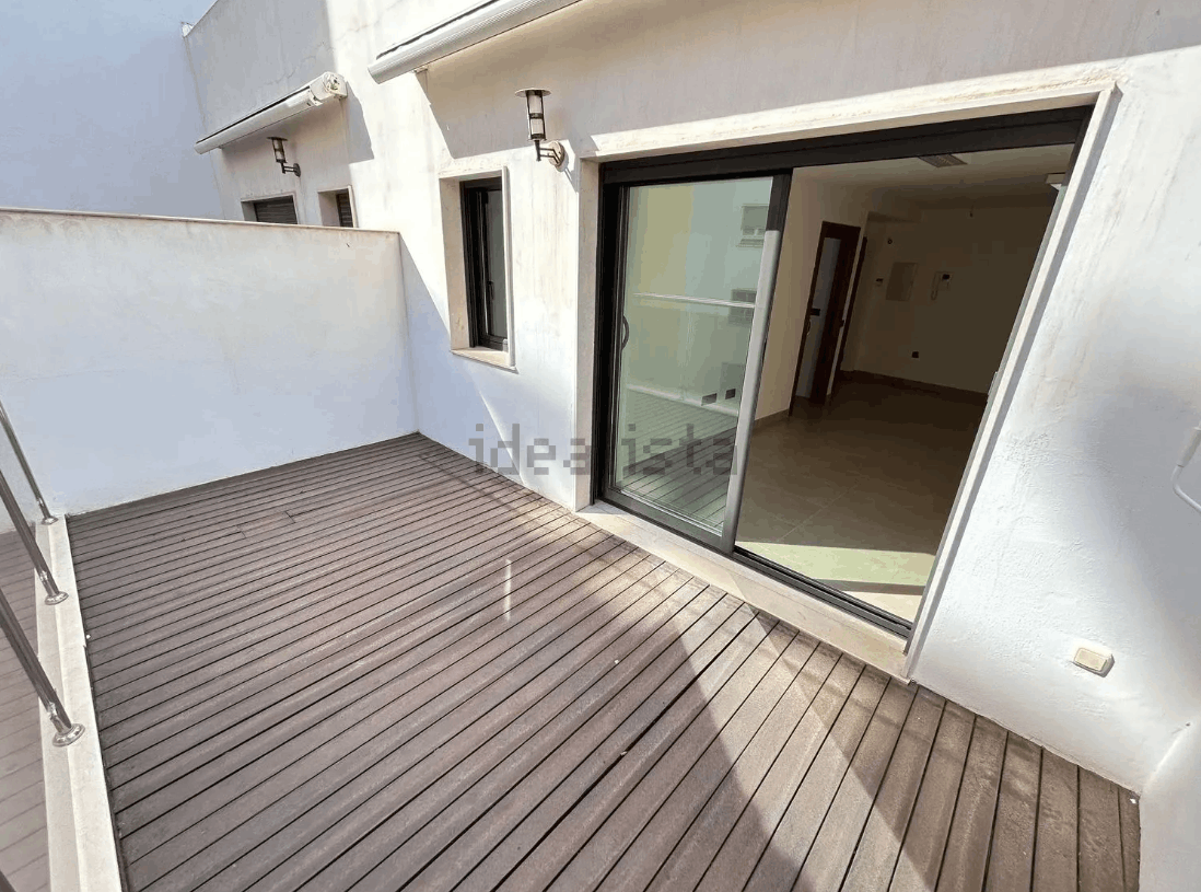 Terraza de madera con puertas corredizas de vidrio abiertas que conducen a un interior de paredes blancas.
