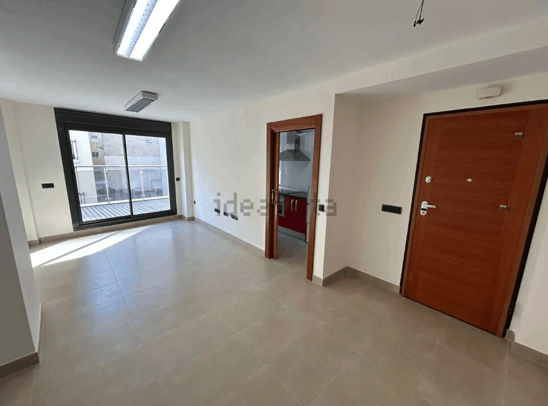 Interior de apartamento vacío con puertas correderas, puerta de la cocina y puerta principal. Suelo beige y paredes blancas.