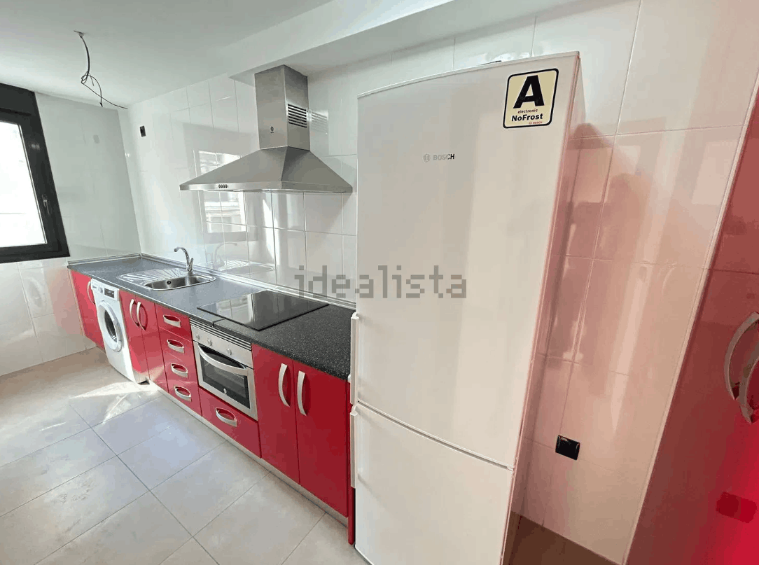 Cocina en tonos rojos y blancos con electrodomésticos, incluyendo refrigerador y horno. Encimeras de granito.