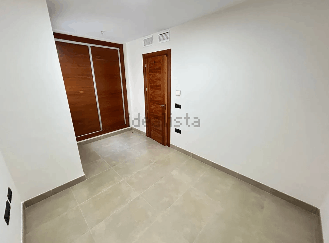 Habitación vacía con suelo y paredes de color claro. Armario y puerta de madera marrón a ambos lados.