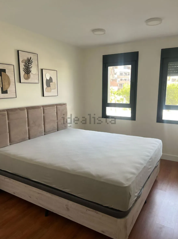 Dormitorio con cama grande, arte en la pared y ventanas con marcos negros.