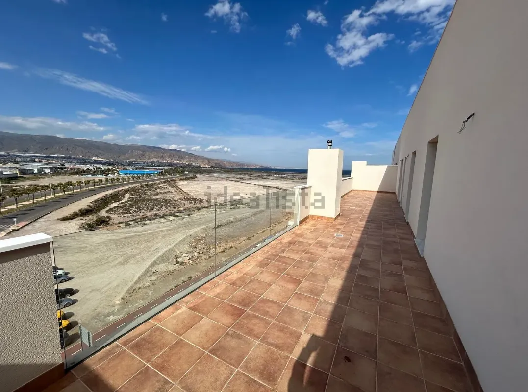 Patio en la azotea con suelo de baldosas, con vista a un paisaje con montañas, edificios y un cielo azul claro.