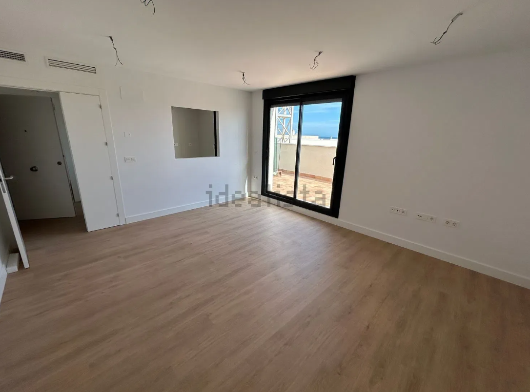 Habitación vacía con pisos de madera, puertas de balcón y una pequeña ventana cuadrada.