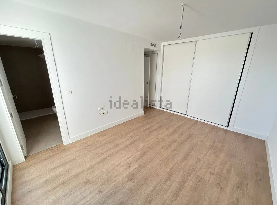 Habitación vacía con suelo de madera, paredes blancas y un armario grande. Puertas a la izquierda y al fondo.