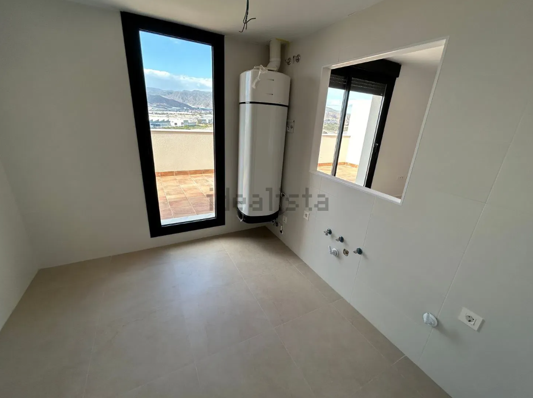 Habitación vacía con un calentador de agua alto, una ventana y una pequeña abertura. 