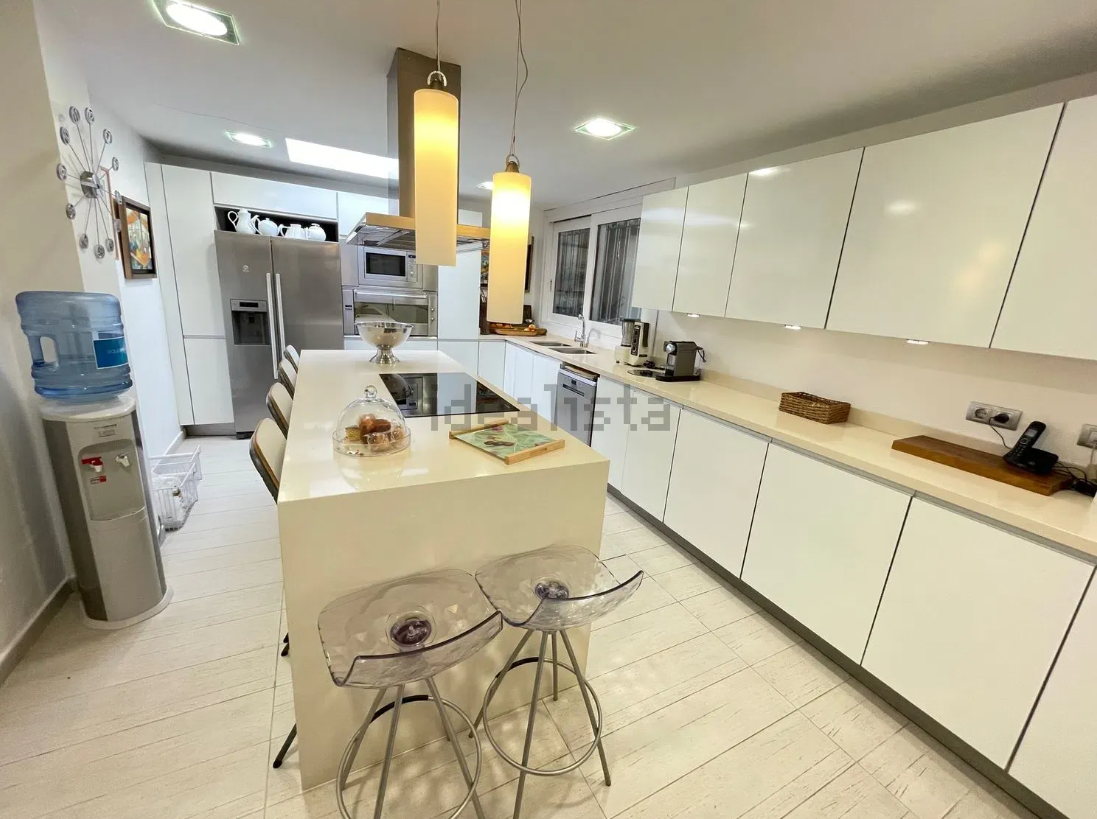 Cocina blanca moderna con una isla grande, taburetes de bar y electrodomésticos de acero inoxidable.