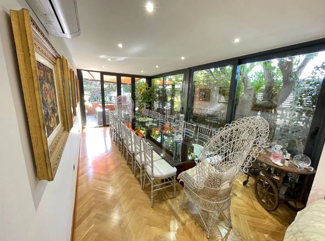 Elegante comedor con mesa larga, sillas y vista al jardín a través de grandes ventanales.