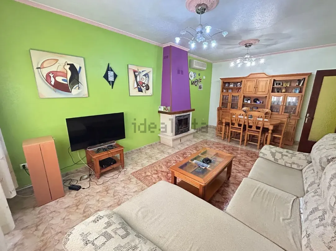 Sala de estar con paredes verdes, TV, chimenea y comedor.