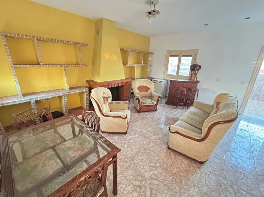 Sala de estar de paredes amarillas con muebles desiguales: un sofá, dos sillones, una mesa de madera y una chimenea.