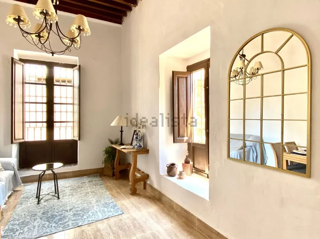 Interior de habitación con espejo arqueado, ventanas con contraventanas, alfombra y lámpara de araña.